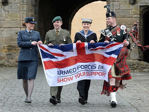Photo of four individuals representing the RAF, Army and Navy holding the Armed Forces Day flag